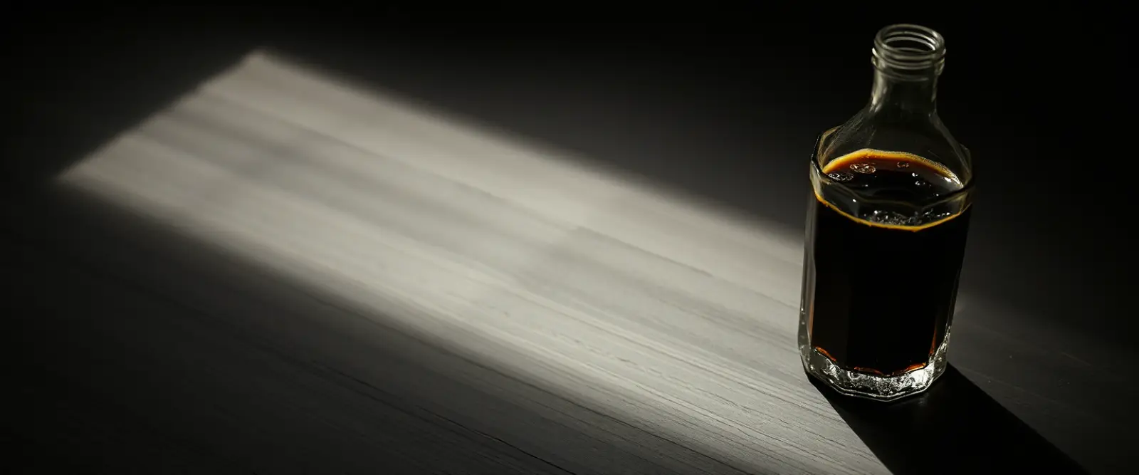 An unlabelled glass bottle and a cut-glass tumbler of a very dark drink.