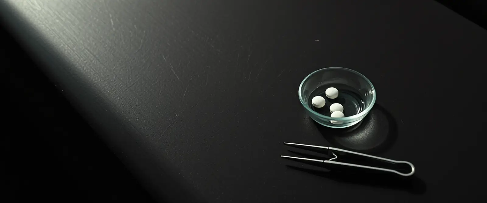 A few plain white tablets in a small glass dish beside steel tweezers.