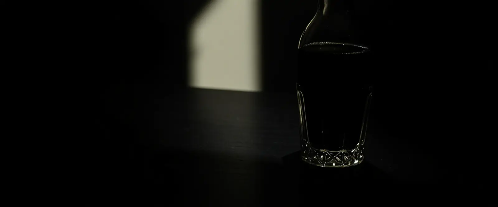 An unlabelled glass bottle and a cut-glass tumbler of a very dark drink.