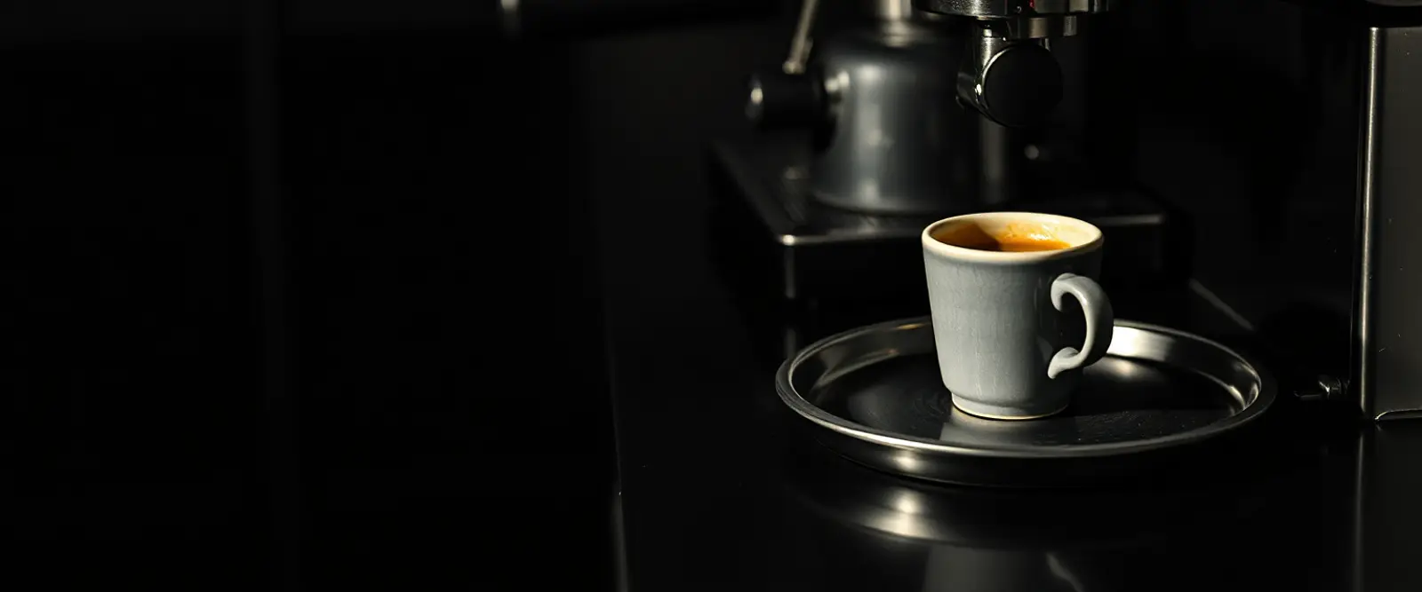 A small espresso cup on a steel tray beside a bare portafilter.