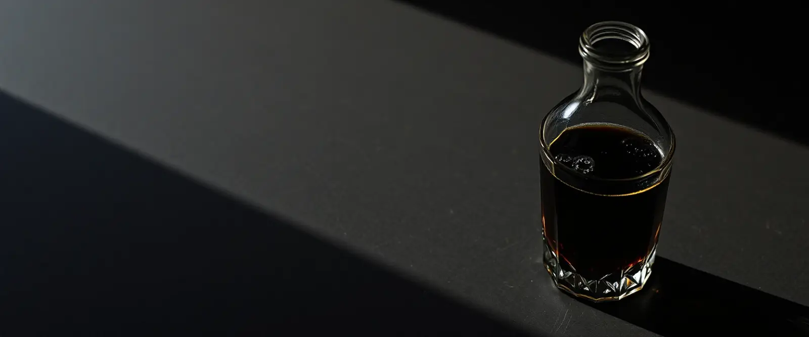 An unlabelled glass bottle and a cut-glass tumbler of a very dark drink.