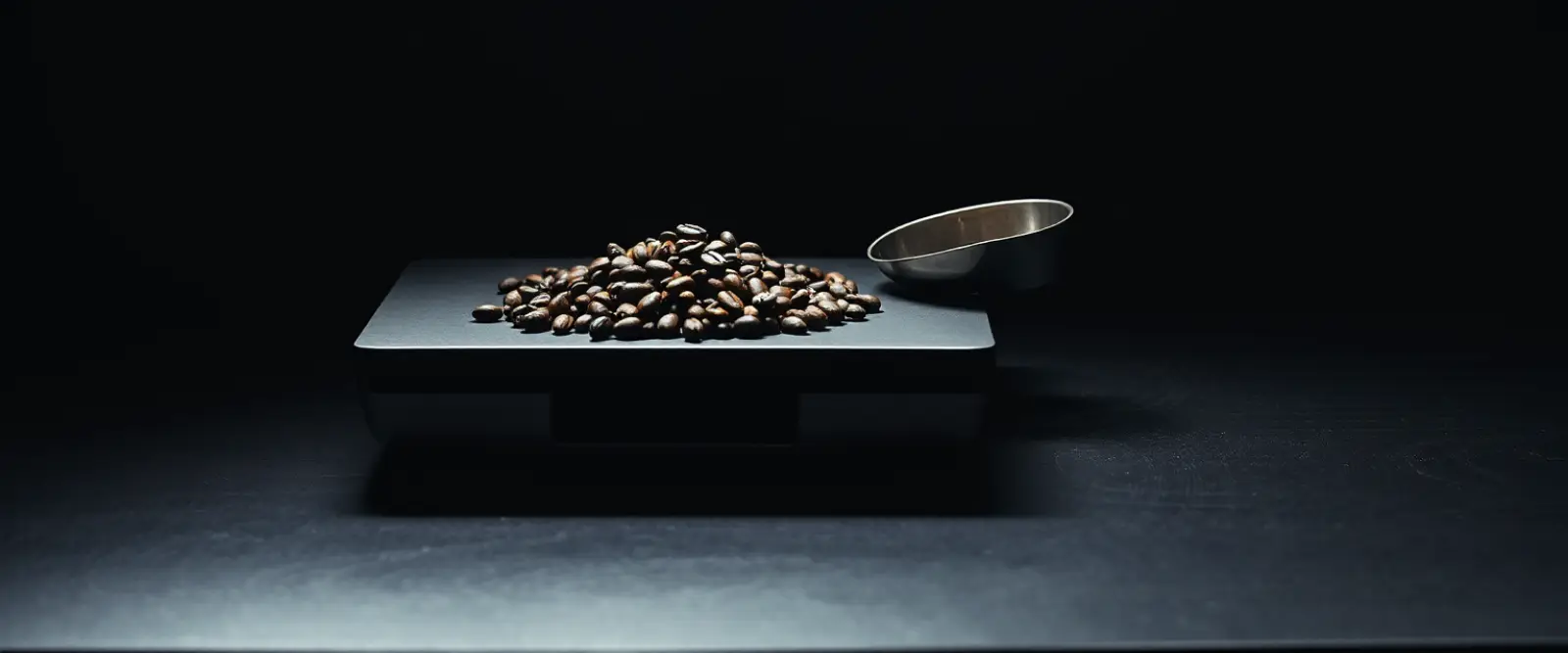 A flat kitchen scale holding roasted coffee beans and a steel scoop.