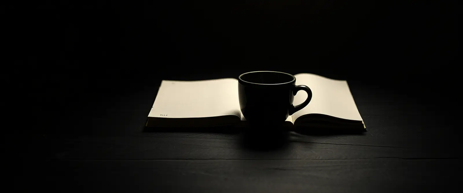 An untouched cup of coffee at the edge of a wide empty table beside a closed notebook.
