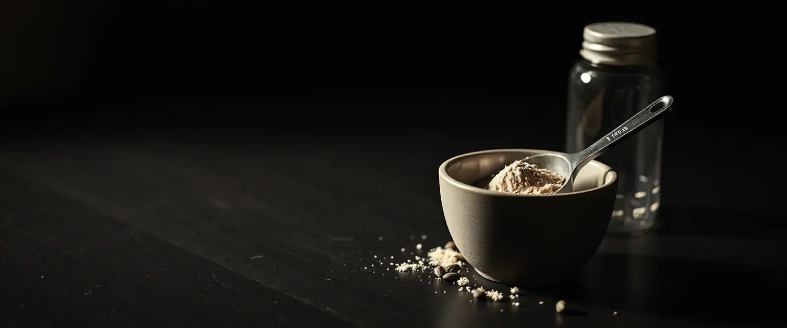A steel measuring scoop of powder in an open tub, a plain shaker bottle behind it.