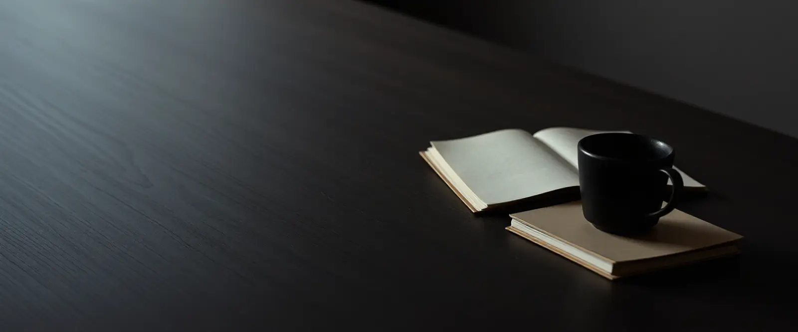 An untouched cup of coffee at the edge of a wide empty table beside a closed notebook.