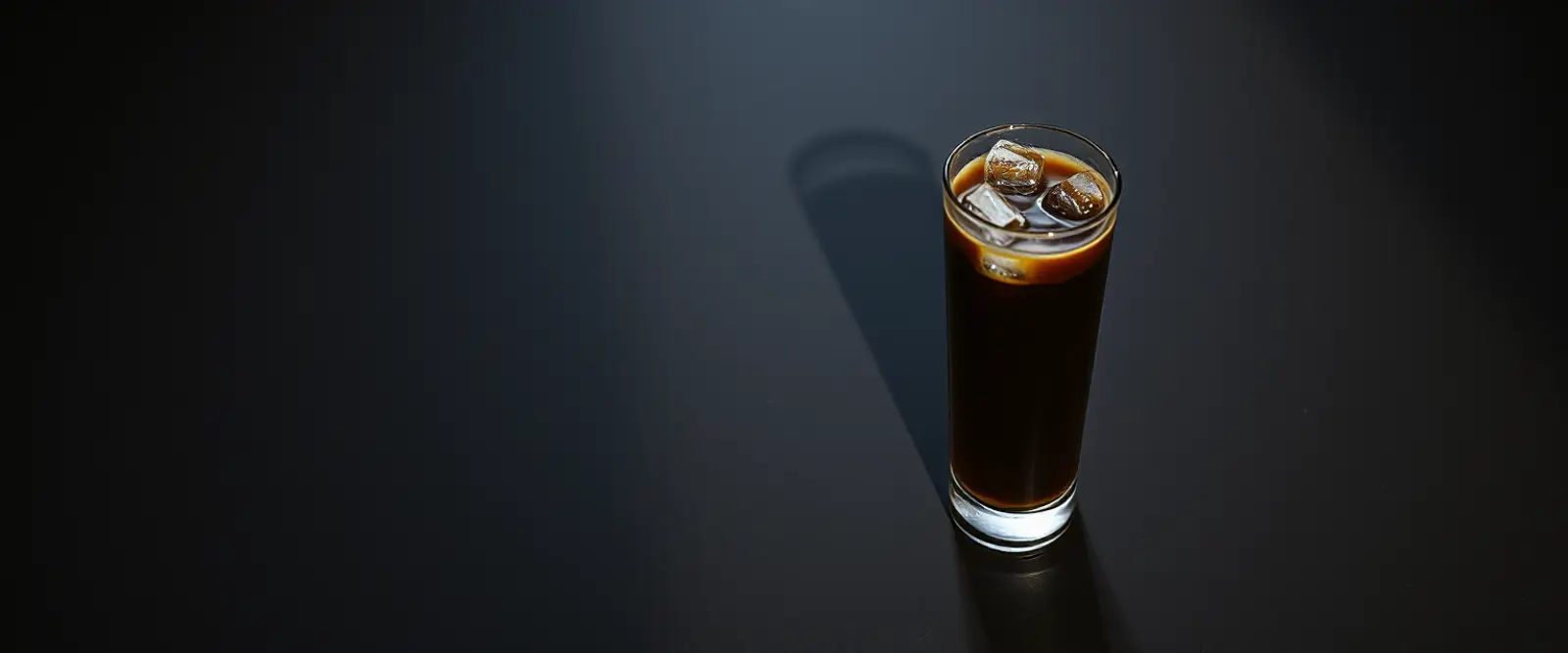 A tall glass of very dark iced coffee on a counter, beaded with condensation.