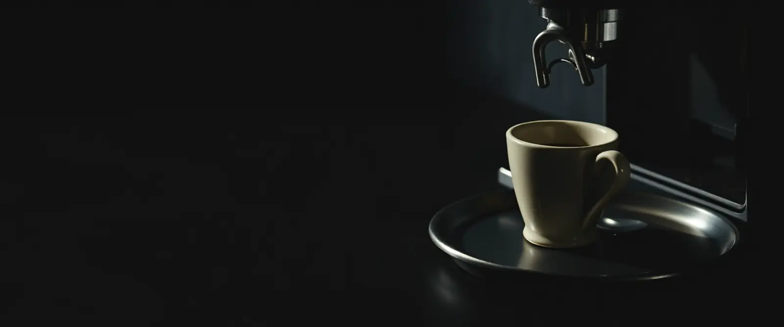 A small espresso cup on a steel tray beside a bare portafilter.