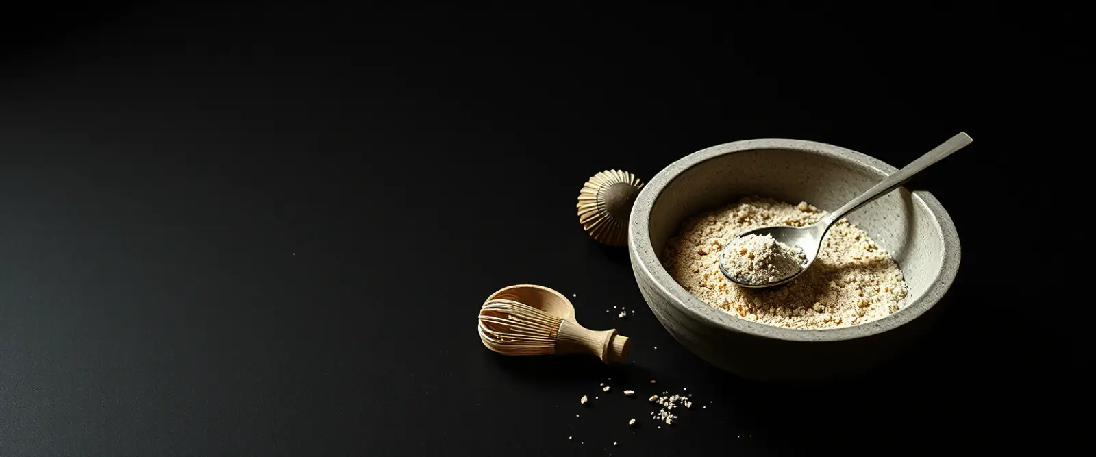 A wide stone bowl of fine tea powder with a bamboo whisk lying beside it.
