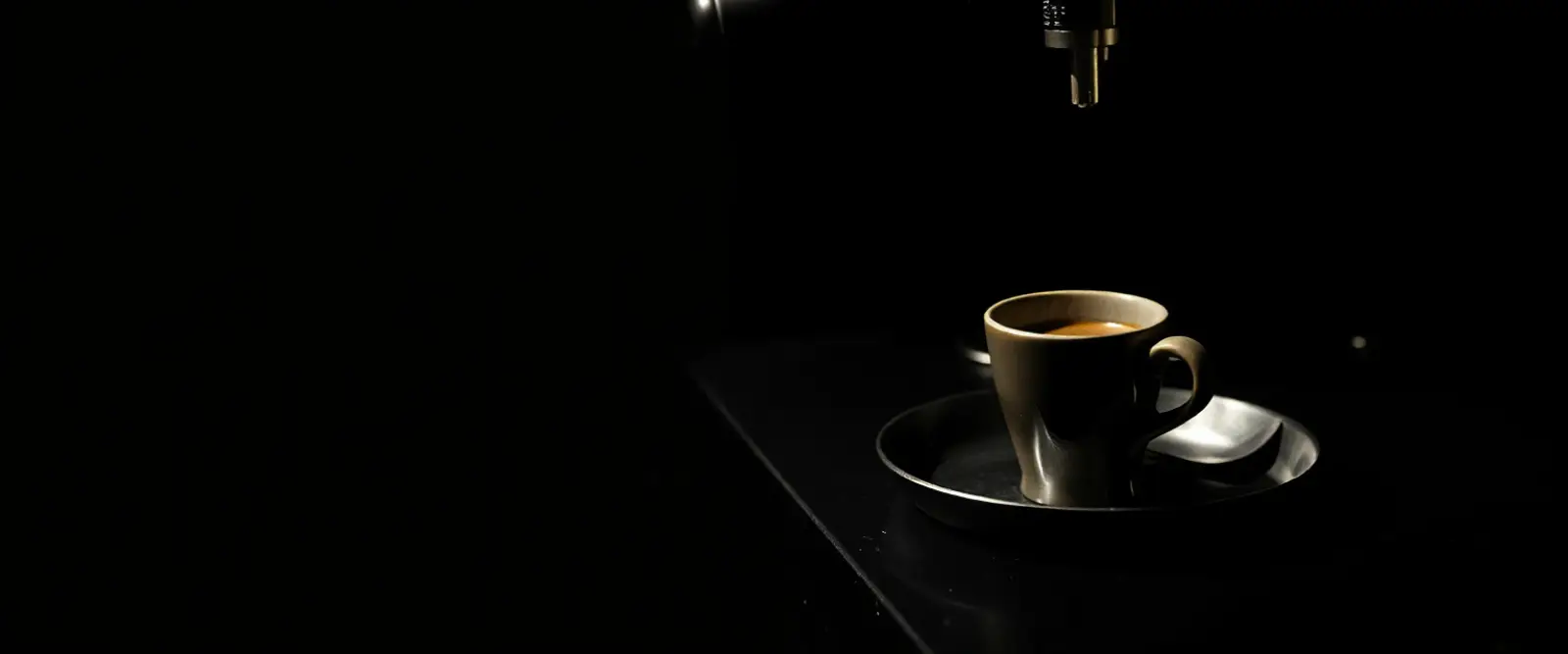 A small espresso cup on a steel tray beside a bare portafilter.