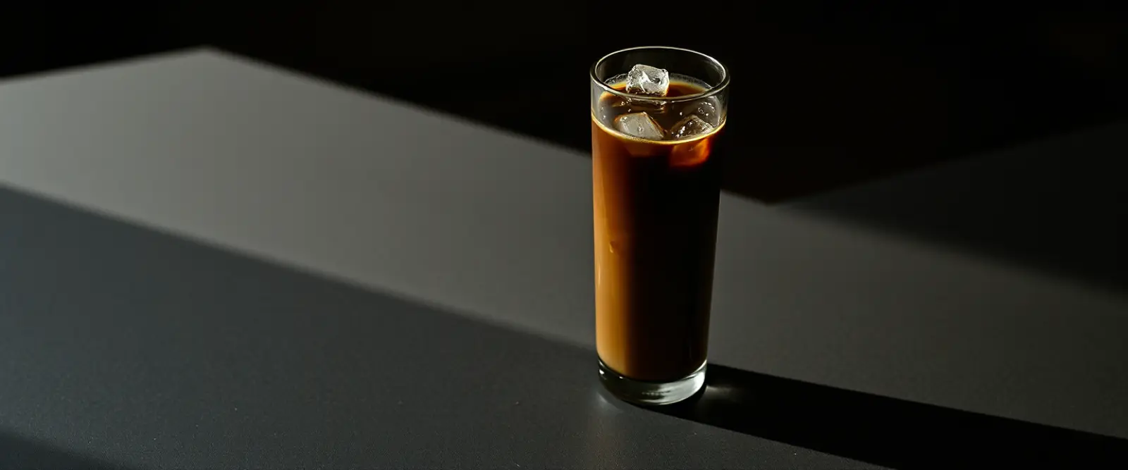 A tall glass of very dark iced coffee on a counter, beaded with condensation.