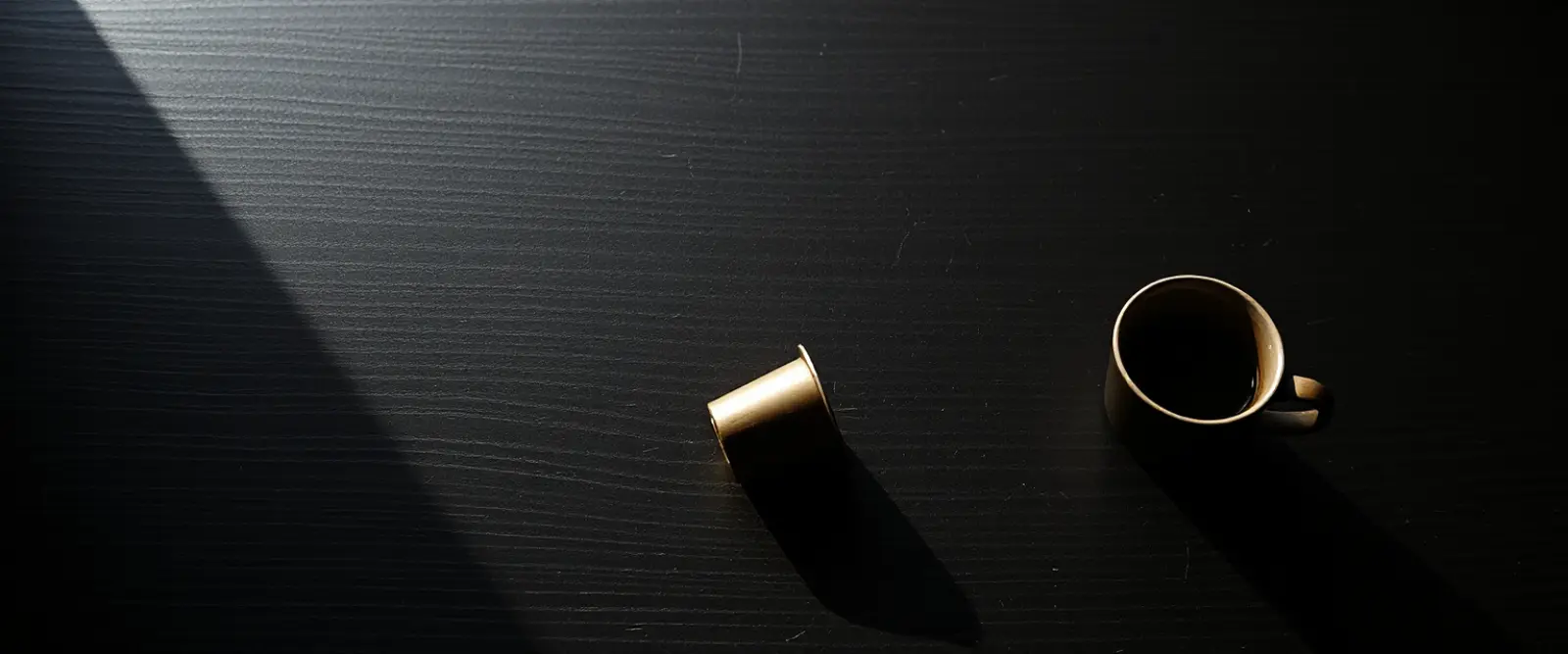 Three coffee capsules and a small dark cup on a table, lit from one side.