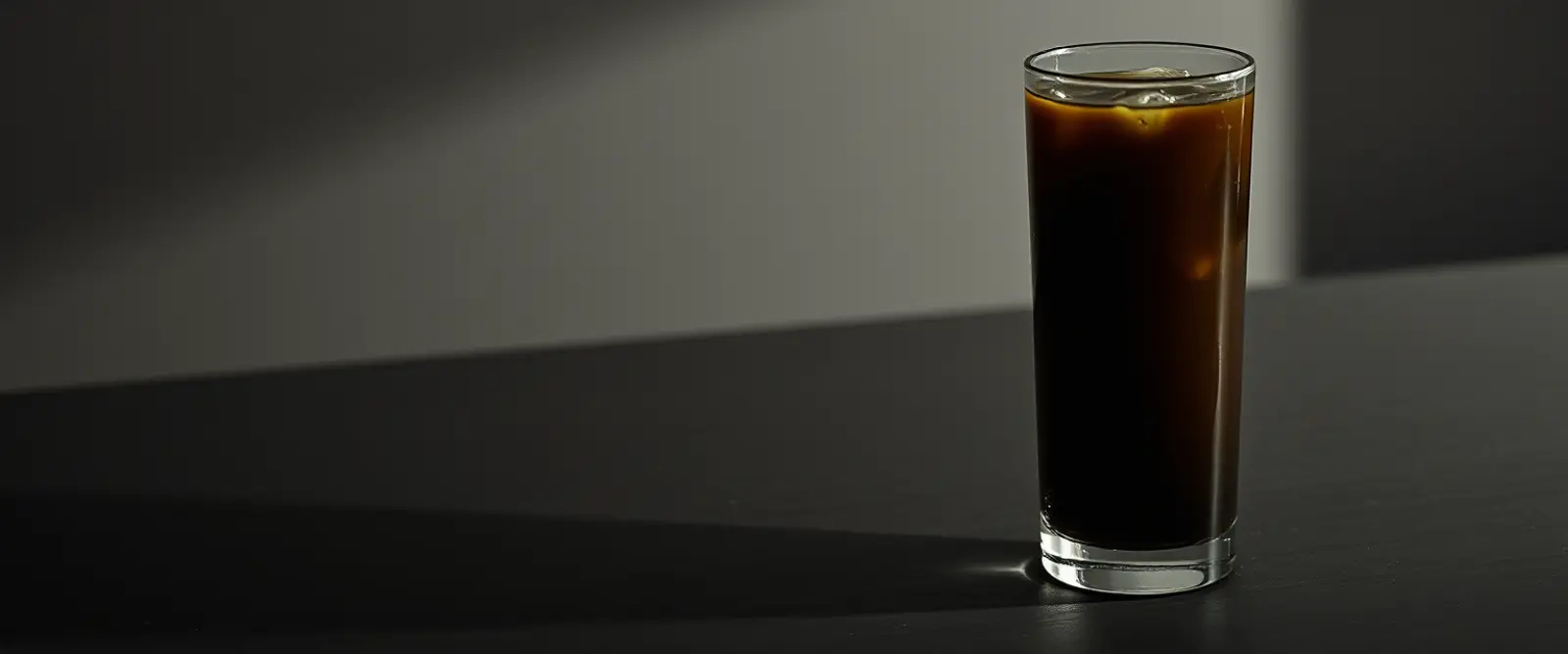 A tall glass of very dark iced coffee on a counter, beaded with condensation.