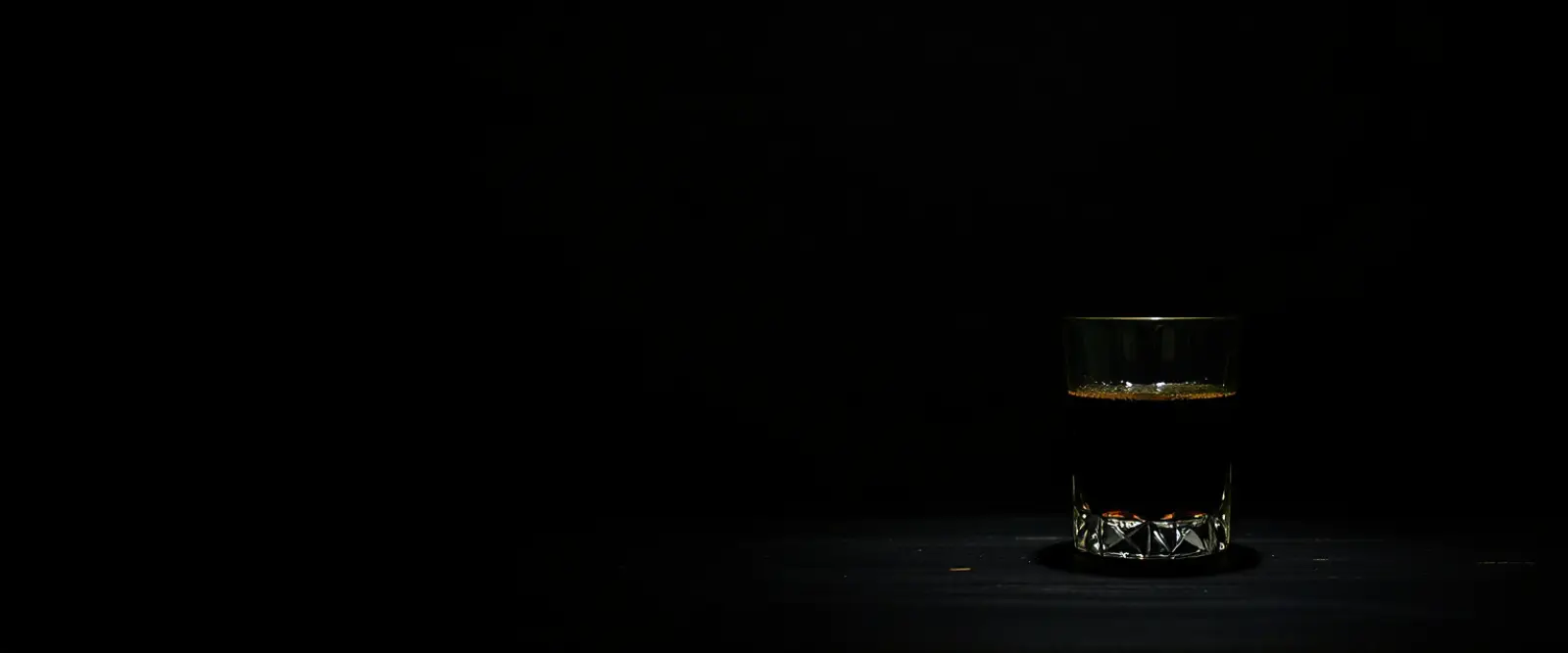 An unlabelled glass bottle and a cut-glass tumbler of a very dark drink.