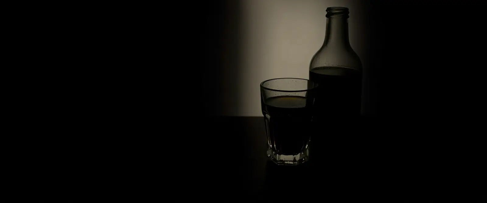 An unlabelled glass bottle and a cut-glass tumbler of a very dark drink.